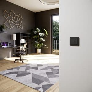 GIRA präsentiert einen Homeoffice-Raum mit einem schwarzen 1fach Wipptaster und grünem Kontrolllampe an einer hellgrauen Wand.