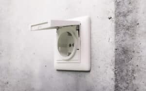 Eine Sichtbetonmauer mit einem SCHUKO-Steckdosensystem in reinweiß glänzend mit Klappdeckel aus dem System 55-Modularprogramm von Gira, das sich für Unterputzinstallation und den kombinierten Einsatz mit passenden Rahmen eignet.