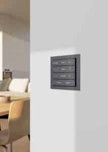 Nahaufnahme eines Gira 4fach-Schalter F200 flach TS4 70 4F in Anthrazit bzw. Schwarz mit Steuerungstasten für Heizung, Jalousie, Downlights und für Wohn- und Eingangsbereich, montiert an einer hellen Wand im modernen Wohnbereich.