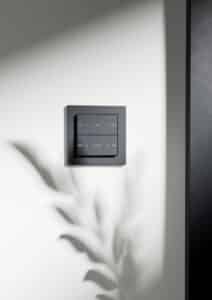 Ein Gira Schalter E2 TS4 55 2F in Anthrazit bzw. Schwarz an einer hellen Wand.