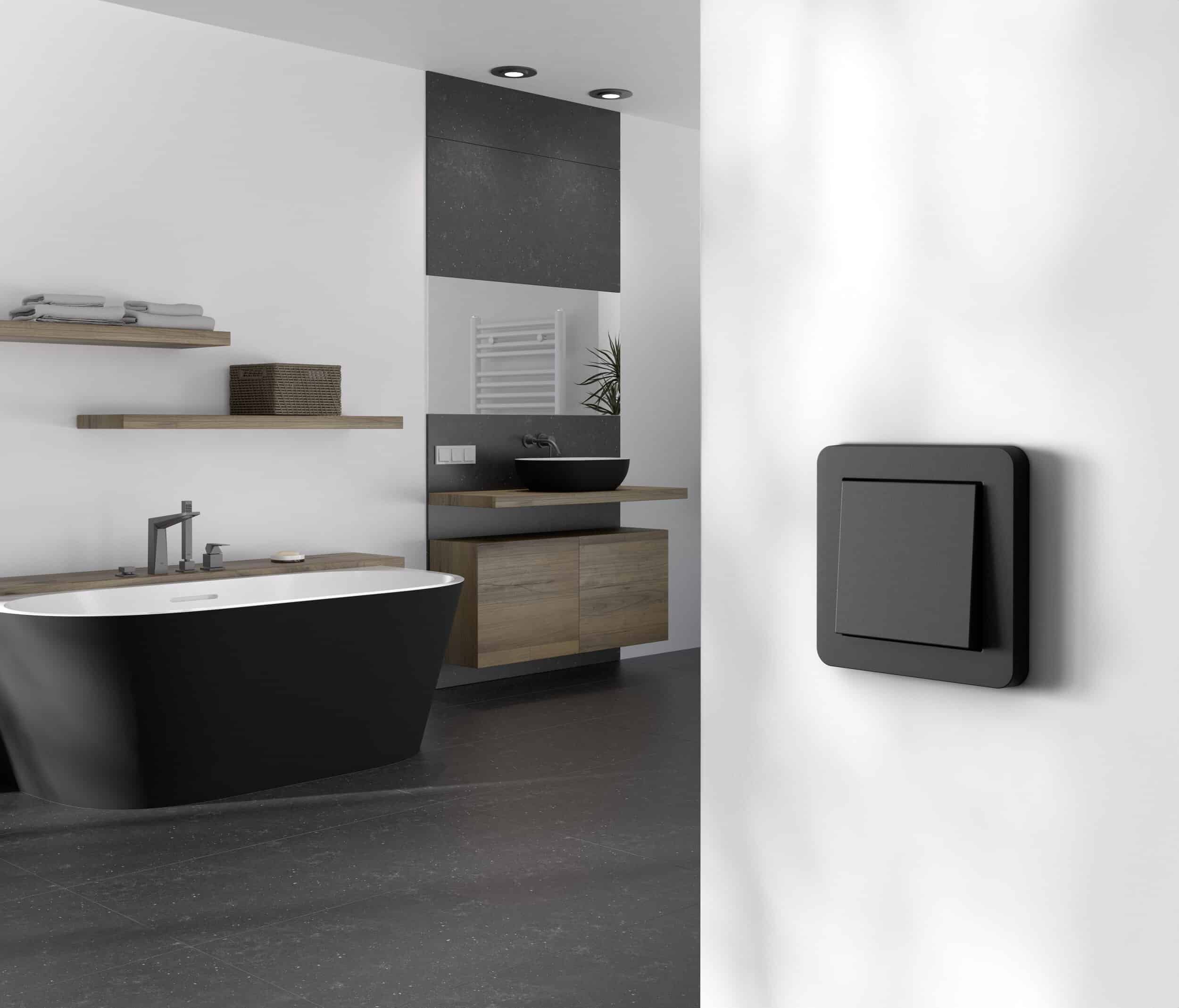 Modernes Badezimmer mit einer freistehenden schwarzen Badewanne, schwebenden Wandregalen und einem Unterbautisch aus Holz, Boden- und Wandfliesen in Anthrazit und einem E1 Schalter in Mattschwarz von Gira.