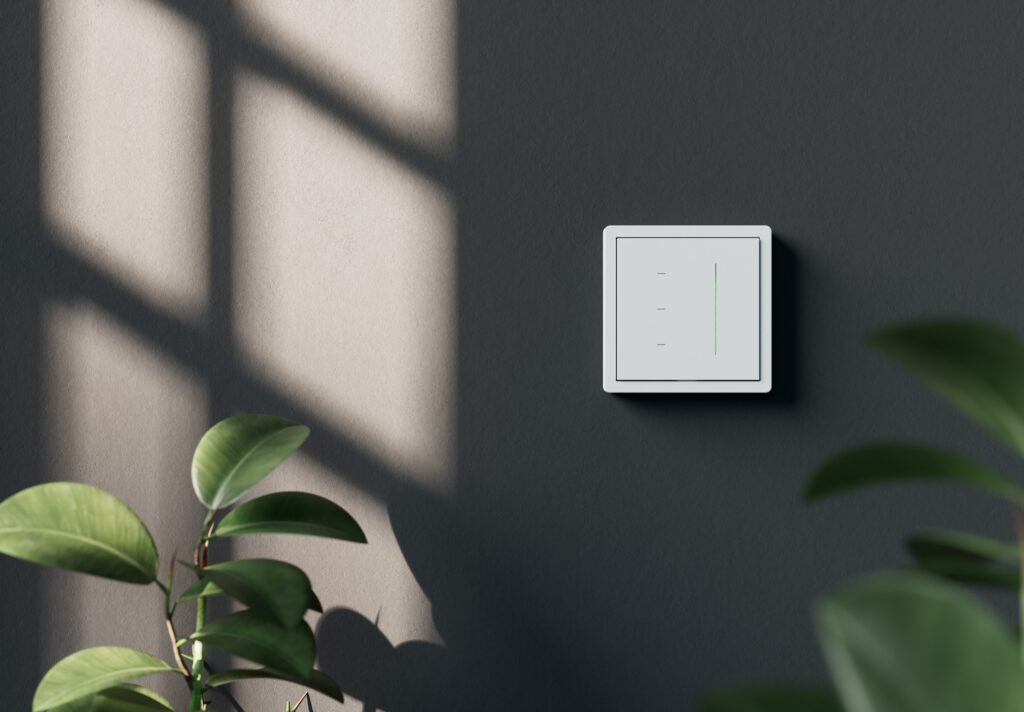 Ein moderner weißer GIRA S3000 Touchschalter an einer dunkelgrauen Wand mit dezenter grüner LED-Anzeige.
