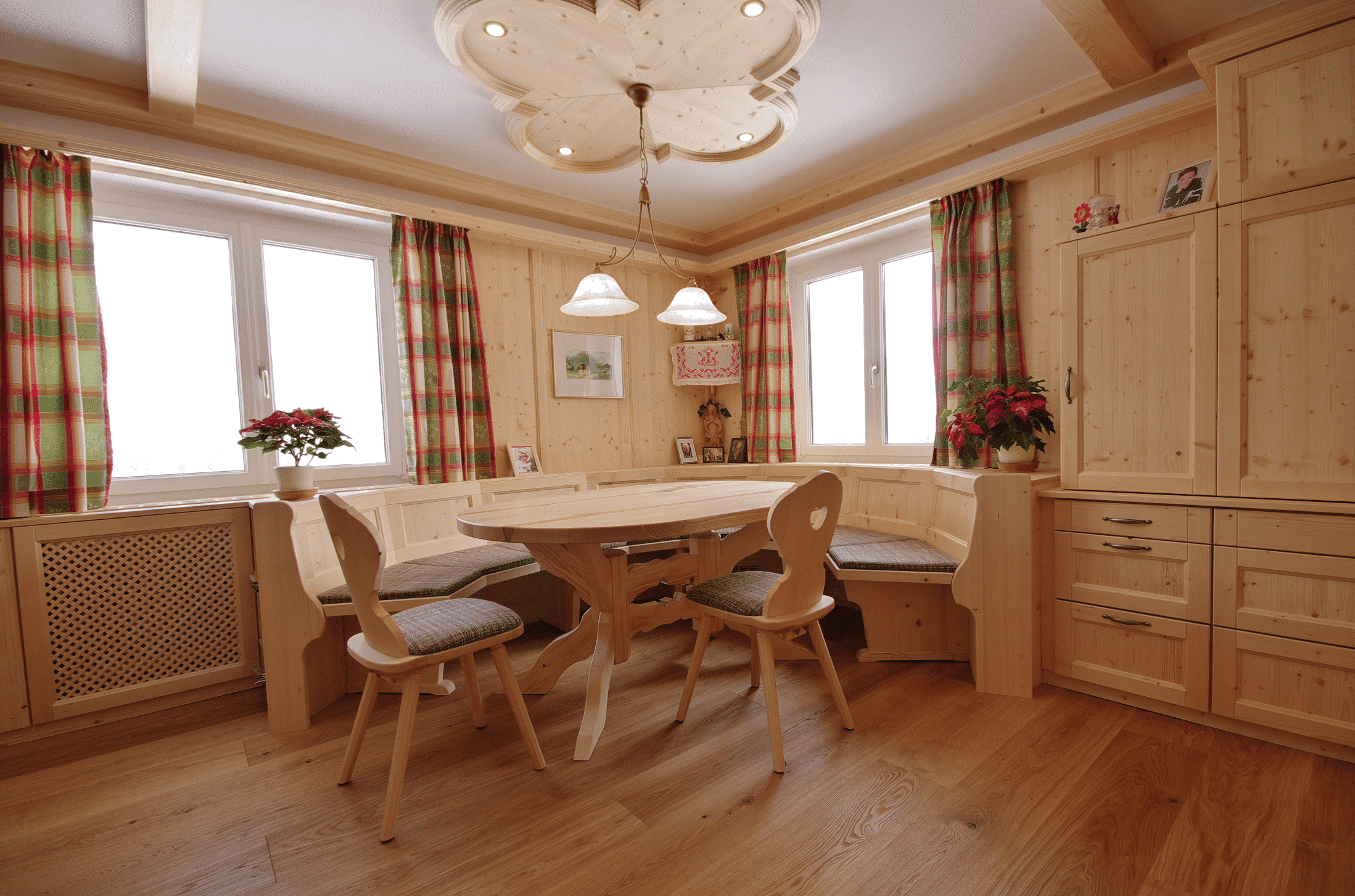 Rustikale Zirbenstube von WOHNHAUS Grill & Ronacher mit uriger Eckbank und Tisch, Einbauschränken und Heizkörperverblendungen aus Holz.