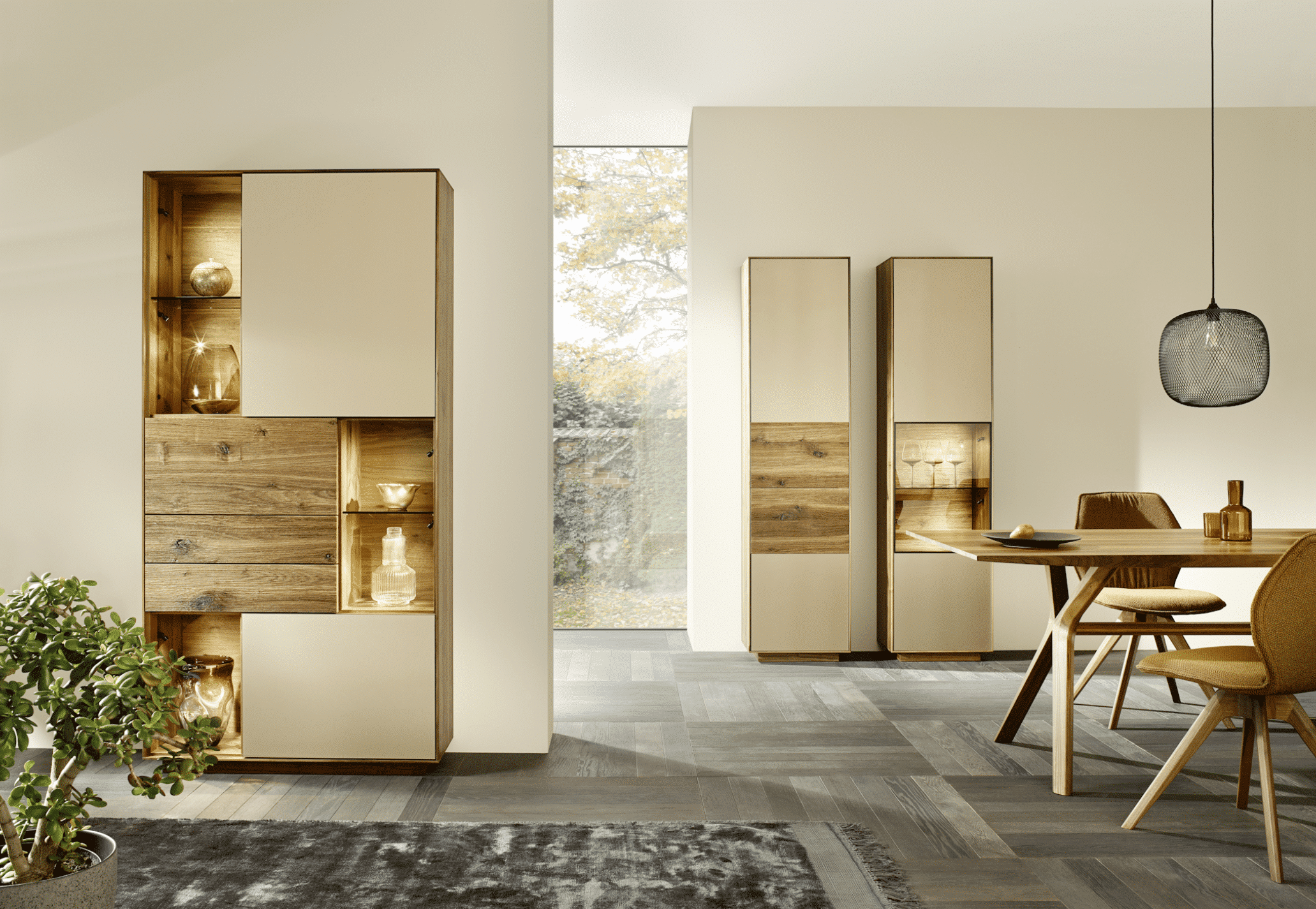 Offener Wohnbereich mit Esstisch und Stühlen aus Holz und Vitrinen mit Holz- und Glaselementen mit Innenbeleuchtung von Grill & Ronacher.