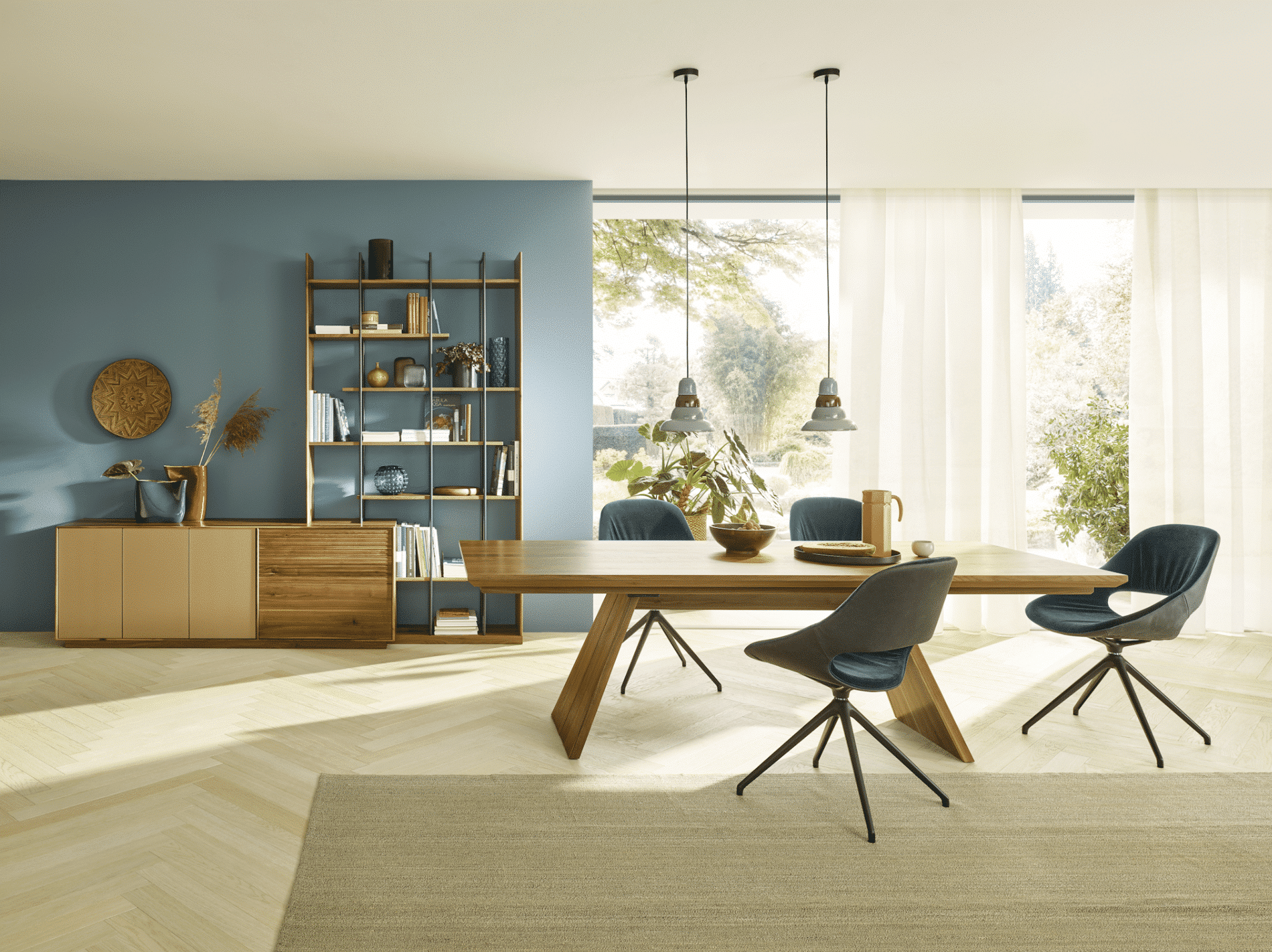 Großzügiger Essbereich mit einem Holztisch und gepolsterten Drehstühlen vor einer Sideboard-Regalkombination aus Holz von Grill & Ronacher.