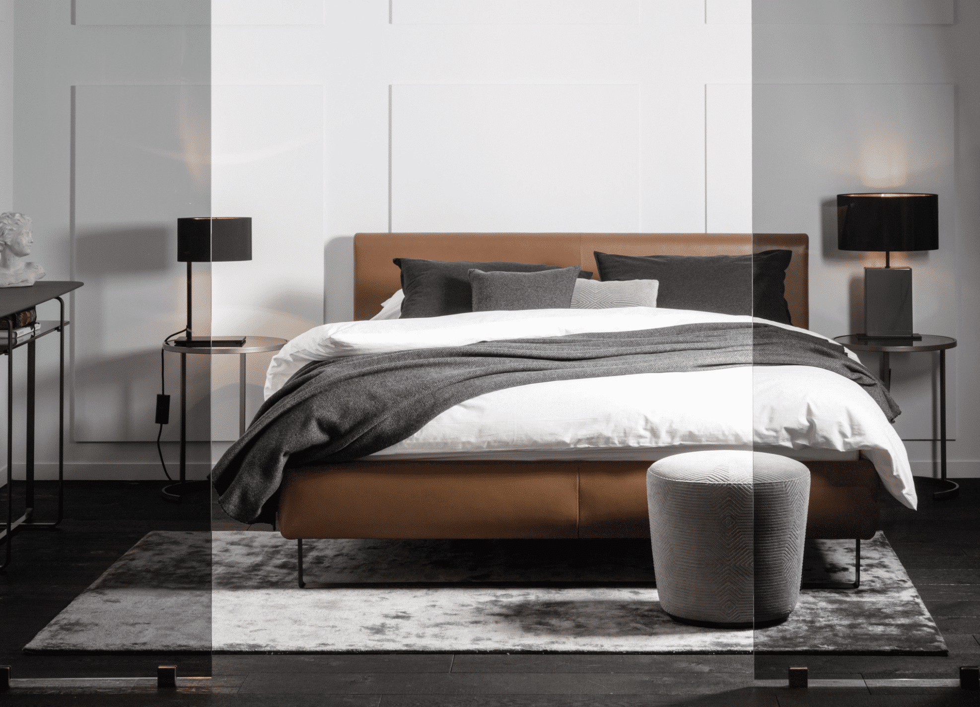 Schlafbereich mit Glastrennwand einem Polsterbett in Rotbraun mit Beistelltischen und Tischleuchten in schwarz von Christine Kroencke Interior Design präsentiert von Grill & Ronacher.