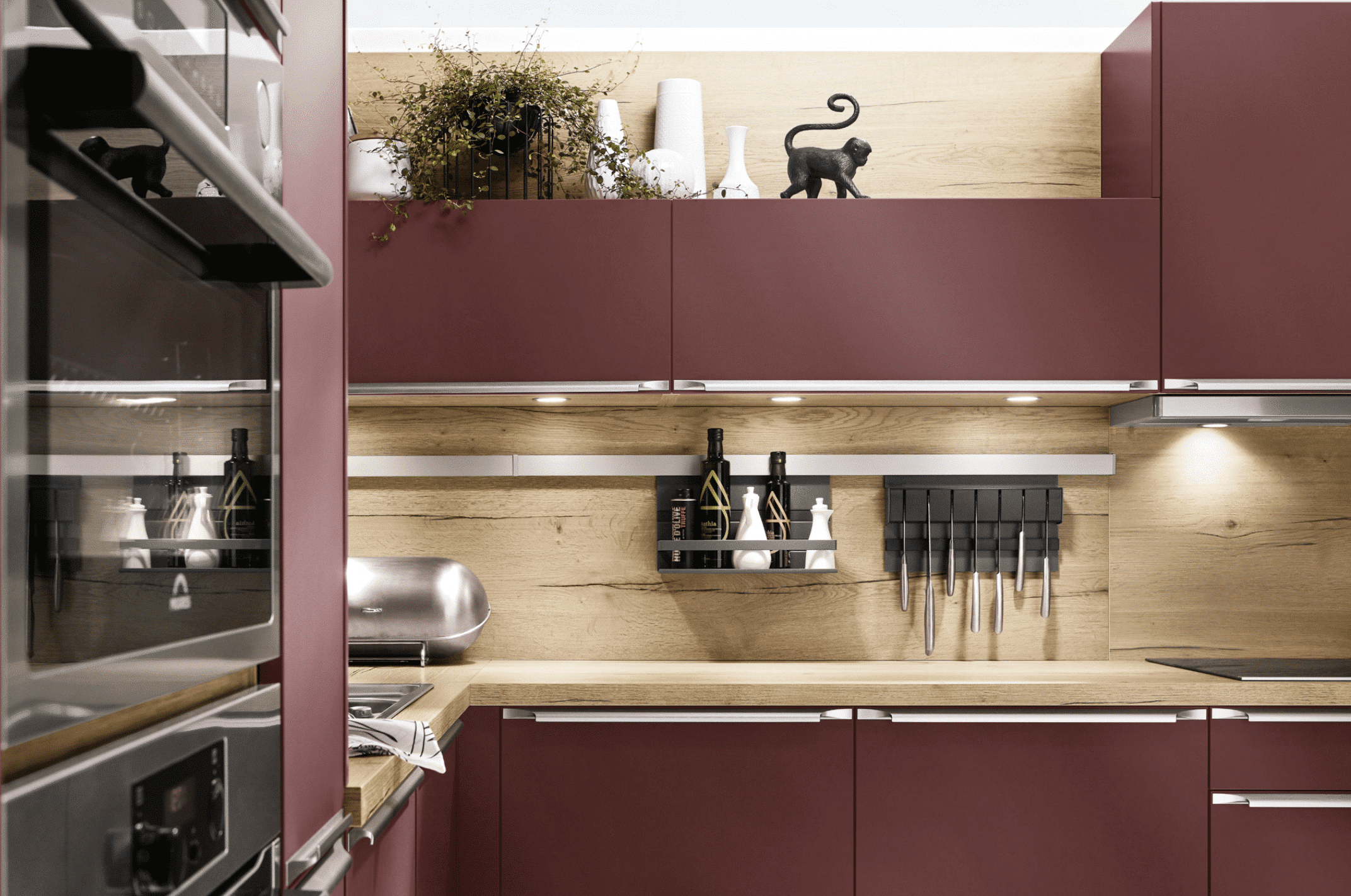 Küche in L-form mit bordeauxroten Fronten, silbernen Griffleisten und einer Arbeitsplatte und Rückwand in Holzoptik von Nobilia präsentiert von Grill & Ronacher.