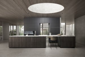 WOHNHAUS Grill & Ronacher zeigt eine Inselküche mit dunklem Holzkorpus, Marmorarbeitsfläche und einer Barfunktion mit Barhockern und dunkelgrauem Wandverbau von Leicht Küchen.