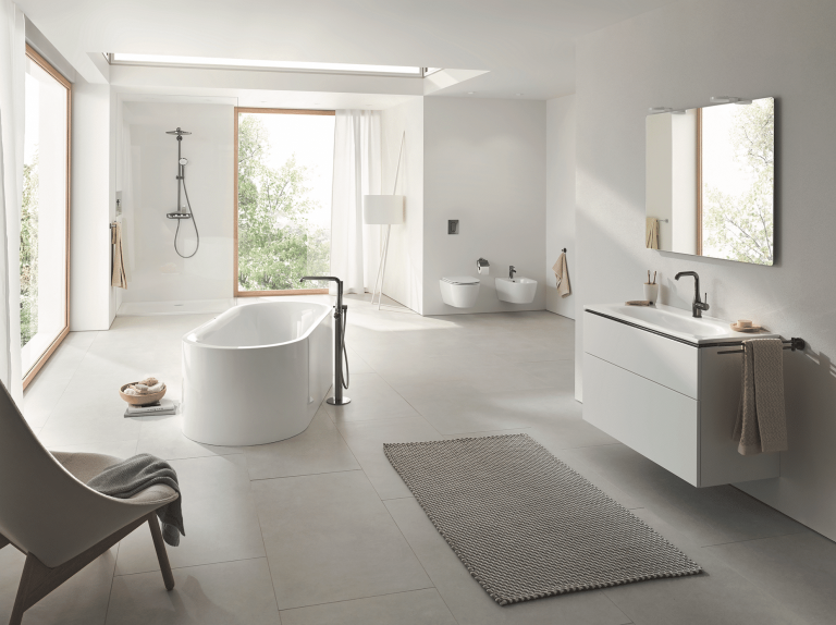 Grohe zeigt ein lichtdurchflutetes Badezimmer in Naturtönen mit einer freistehenden Badewanne, offener Dusche und weissem Waschtisch mit silbernen Armaturen und Fliesenboden.
