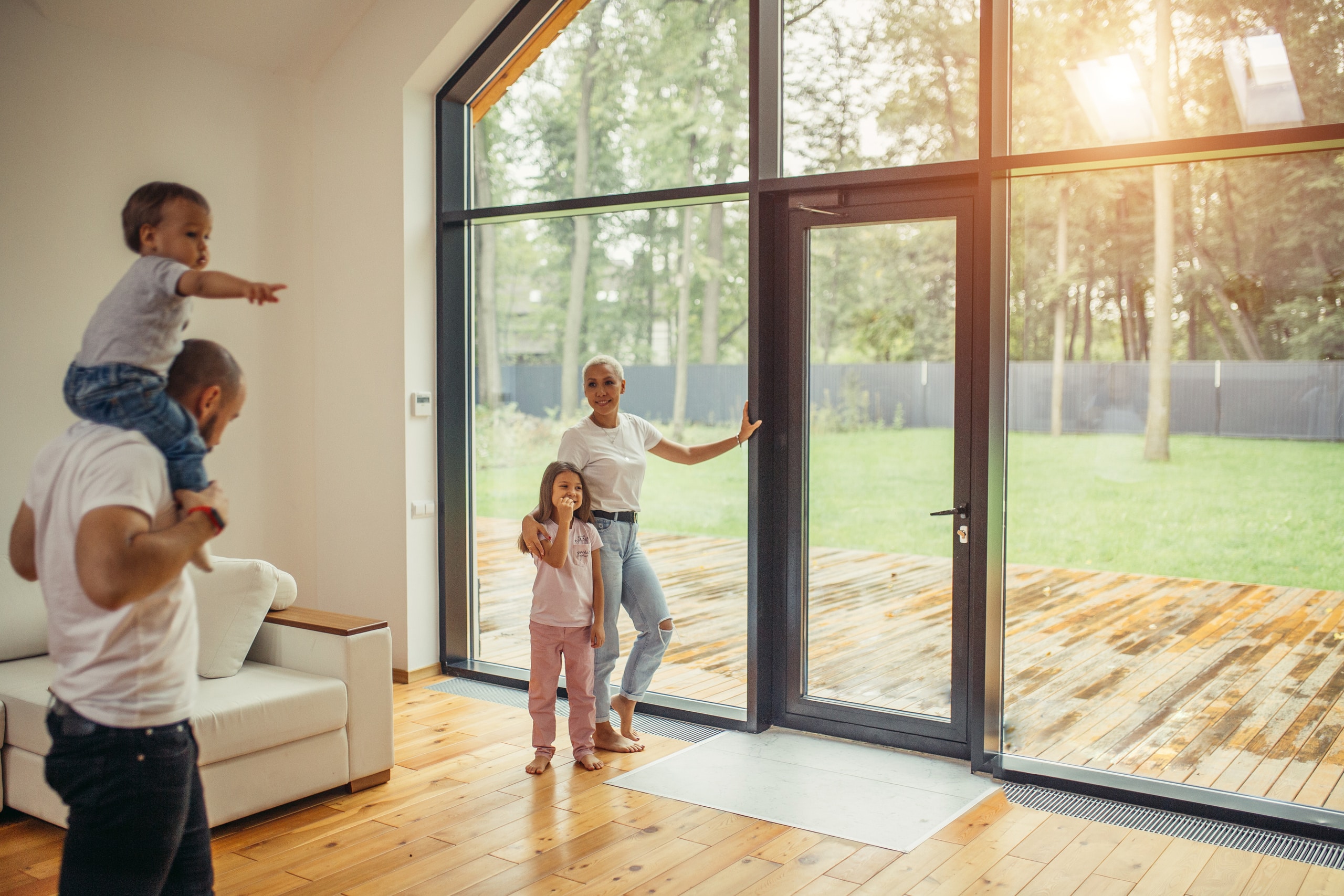 Eine Familie im offenen Wohnraum ihres Hauses mit bodentiefer Vollverglasung und Terrassentür mit schwarzem Alu-Rahmen von Haderer.