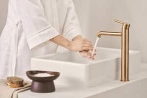 HANSA präsentiert den Wasserhahn mit Drehhebel aus gebürsteter Bronze der Serie Viva, der hinter dem aufgesetzten Waschbecken steht.