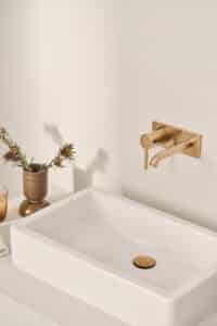 HANSA präsentiert den Wasserhahn mit Drehhebel aus gebürsteter Bronze der Serie Viva, der an der Wand montiert ist, mit passender Abflussabdeckung.