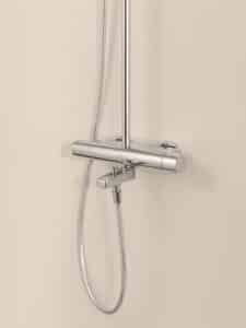 HANSA zeigt die verchromte glänzende Wandarmatur Viva mit Thermostat-Drehregler und angeschlossener Handbrause.