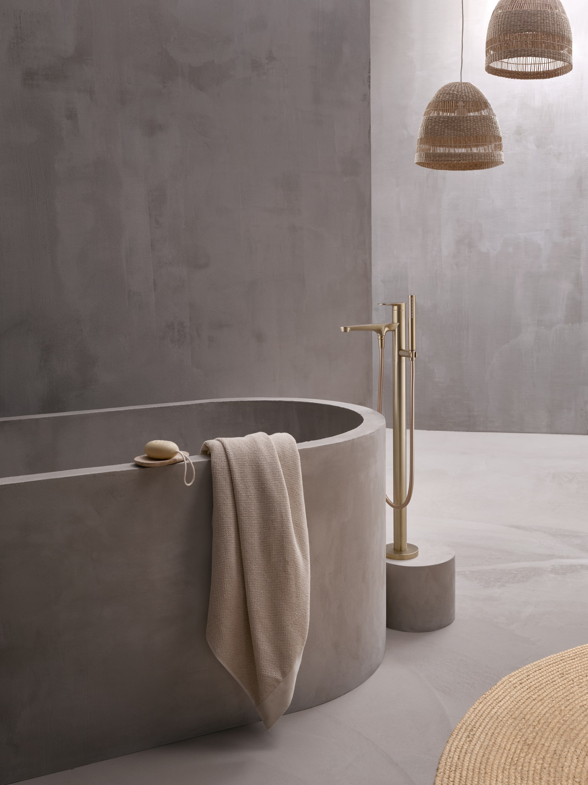 Hansa zeigt eine moderne freistehende Badewanne mit einer freistehenden Armatur in gold mit obenliegendem Hebel und mit stabförmigen Handdusche, auf einem Sockel montiert.