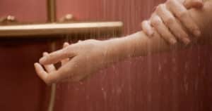 Hansa zeigt eine Frau, die sich den Arm wäscht in einer Dusche mit messingfarbener Wandarmatur.