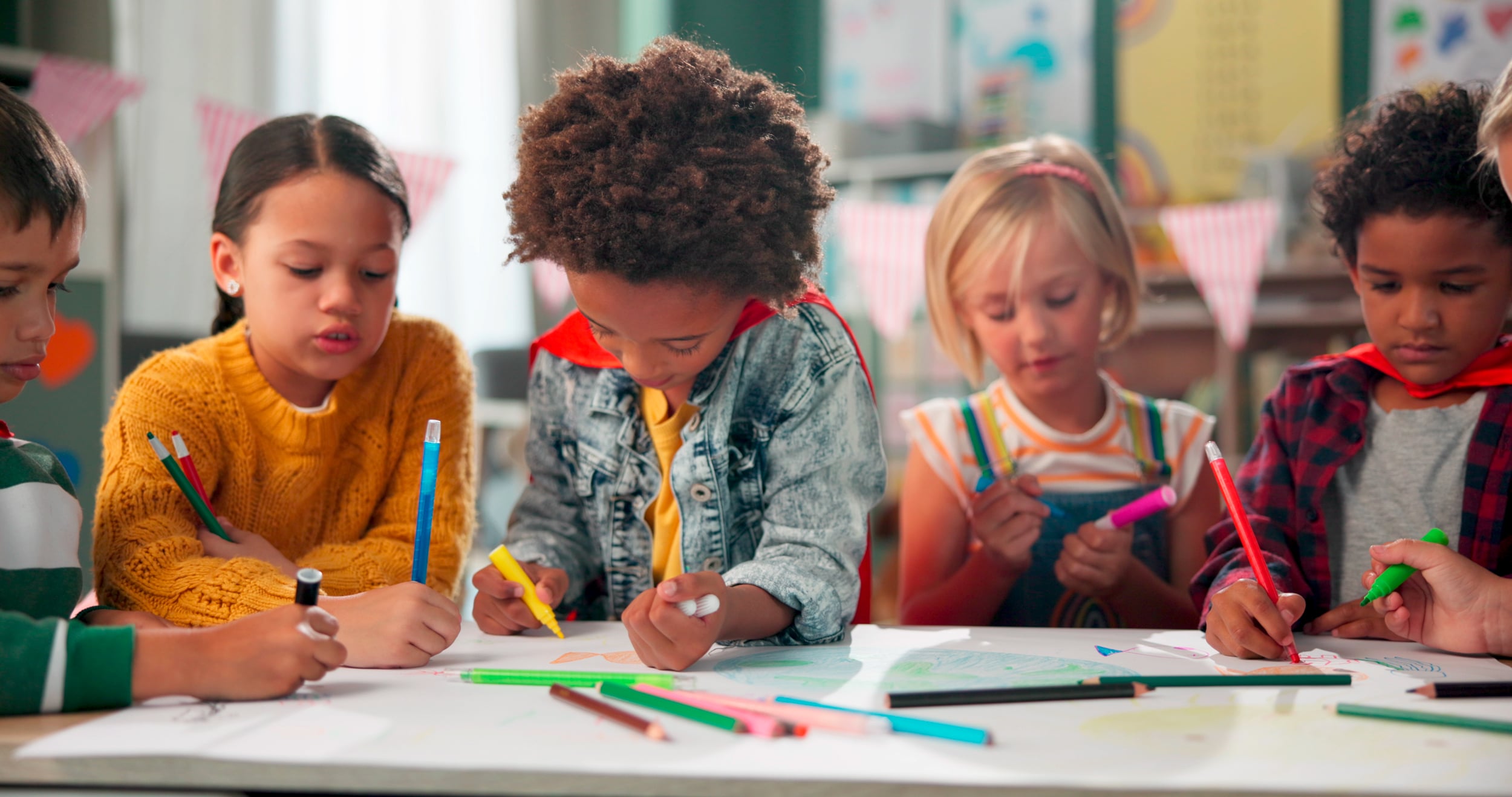 Fröhliche Kinder sitzen gemeinsam an einem Tisch und malen.