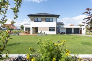 HARTL HAUS zeigt ein zweistöckiges Einfamilienhaus mit Zeltdach, Doppelgarage, großer Terrasse und Garten.