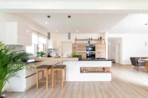 HARTL HAUS zeigt eine offene Wohnküche mit Kochinsel, integrierter Theke und Barhockern.