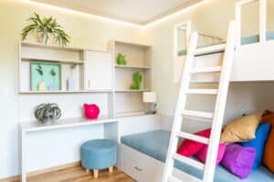Ein helles, freundliches, kompaktes Kinderzimmer mit beleuchteter Deckenleiste und Schreibtisch-Stockbett-Kombination von HARTL HAUS.