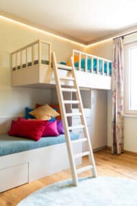 Ein helles, freundliches, kompaktes Kinderzimmer mit beleuchteter Deckenleiste und Stockbett-Kleiderkasten-Kombination von HARTL HAUS.