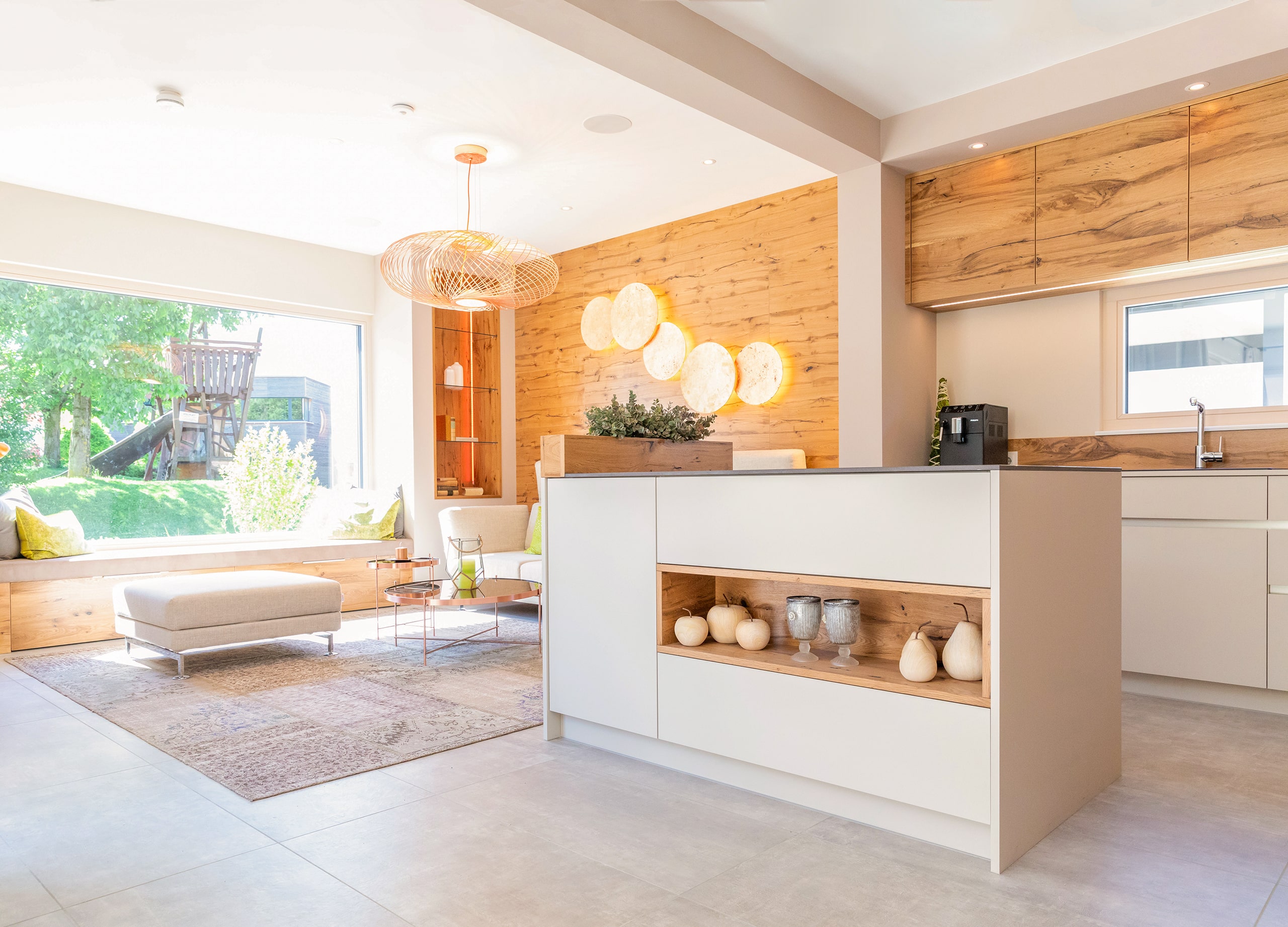 Ein offener Wohn‑ und Essbereich mit maßgeschneiderter Wohnküche, Bar‑Element und Panorama-Sitzfenster von HARTL HAUS.