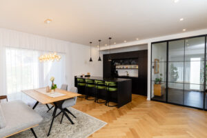 Ein offener Wohn‑ und Essbereich mit Wohnküche, Bar‑Element und großen Glastüren von HARTL HAUS.