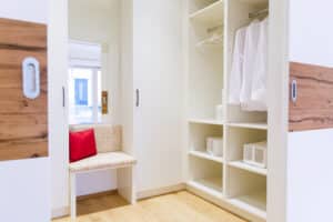 Ein begehbarer Kleiderschrank bzw- Ankleidezimmer mit weißen maßgefertigten Einbauschränken, gepolsterter Sitzgelegenheit und Schiebetüren zum angrenzenden Raum von HARTL HAUS.