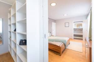Ein begehbarer Kleiderschrank mit weißen Regalen und direktem Zugang zum angrenzenden Schlafzimmer durch eine Schiebetüre von HARTL HAUS.