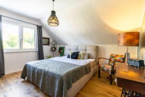 Ein Schalf- bzw. Gästezimmer von HARTL HAUS mit Dachschräge, Lesestuhl und antiker Kommode mit Nähmaschinengestell.