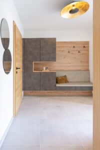 Ein Hauseingang mit einer Wand aus Garderoben- Schrank- und Sitzbankkombination gepolstert und aus Holz von HARTL HAUS.