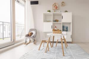 Ein liebevoll eingerichtetes Kinderzimmer mit Regalwand, Schaukelstuhl, Spiel-, Mal bzw. Lernbereich mit gemütlichem Kindertisch und zwei Stühlen und Balkonzugang durch Hebeschiebetüren von HARTL HAUS.