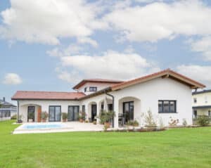 Ein klassisch-mediterranes Haus mit rotem Ziegeldach, überdachtem Terrassenbereich mit Rundbogendurchgängen und Pool von HARTL HAUS.