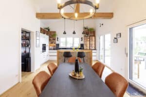 Ein klassisch-rustikaler Wohnküchen- und Essbereich mit Holzbalken, stilvollen Hängeleuchten, Terrassenschiebetüren und Einblick in die Speisekammer von HARTL HAUS.