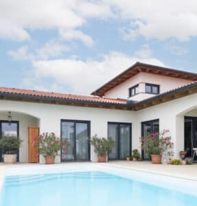 Ein klassisches Haus mit roten Dachziegeln, Rundbögen, überdachter Terrasse und Pool in mediterranem Stil von HARTL HAUS.