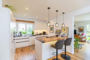 Eine moderne Wohnküche mit Einbauküche, integrierter Bar und offenem Blick in den angrenzenden Wohnbereich von HARTL HAUS.
