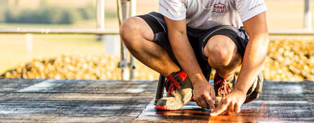Ein Arbeiter von HARTL HAUS markiert präzise eine Fläche auf einer Baustelle im Freien.