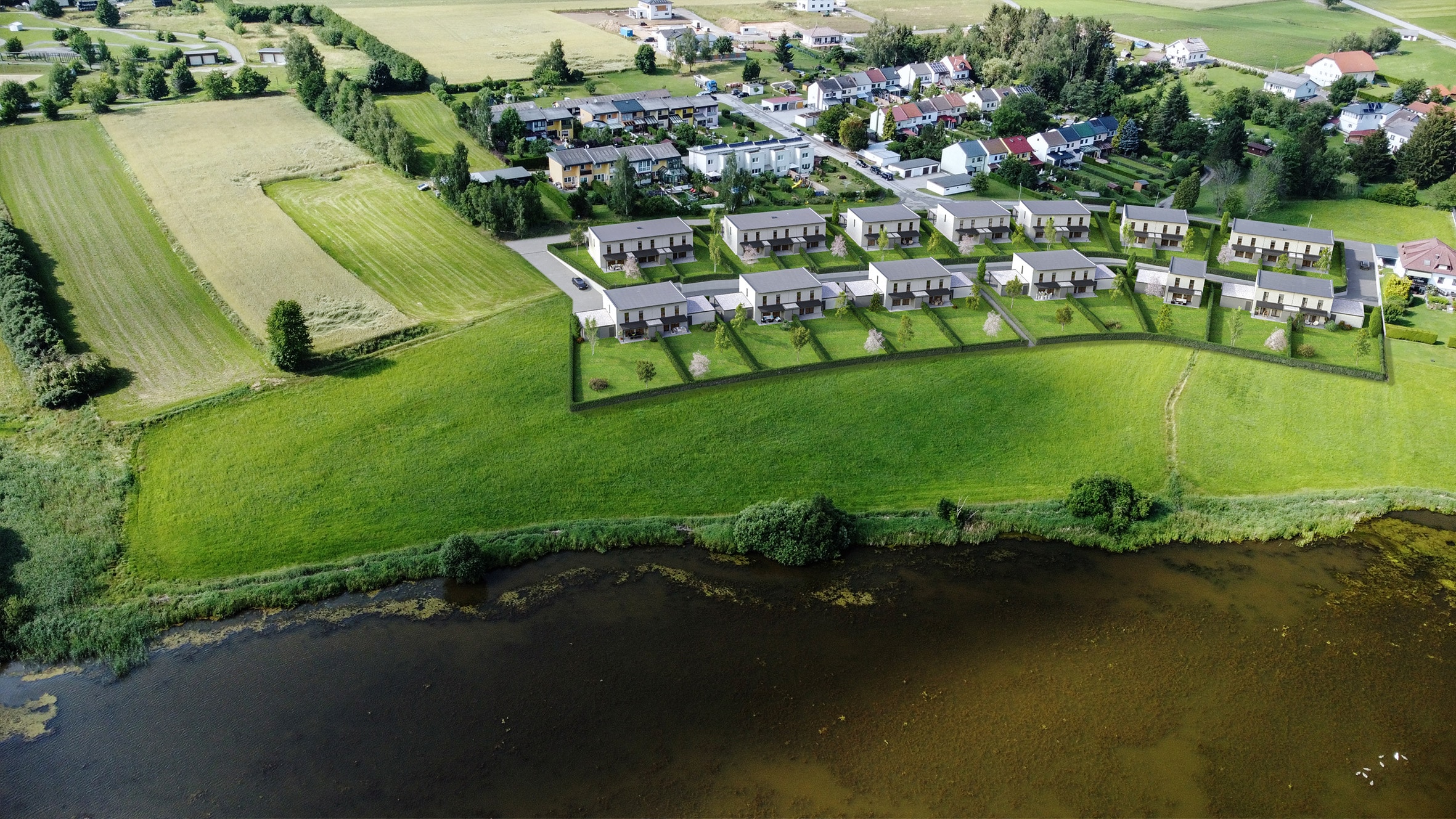 Luftaufnahme einer modernen Reihenhaussiedlung an einem Ufergrundstück in Heidenreichstein, umgeben von grünen Gärten und Feldern von HARTL HAUS.