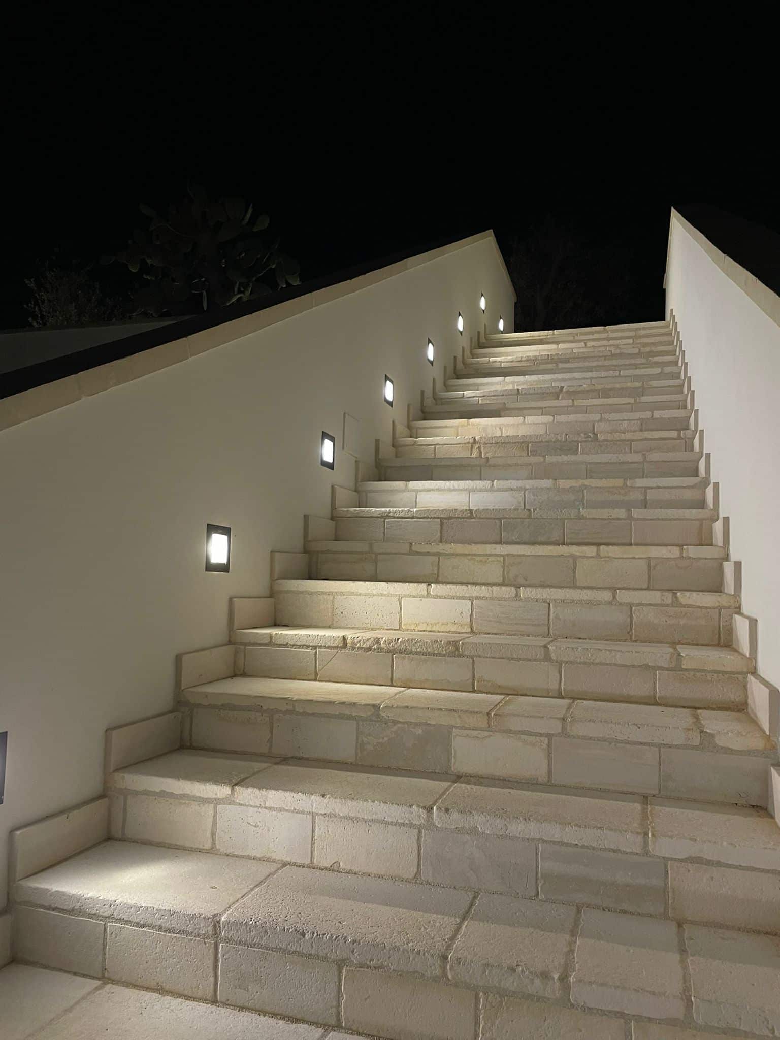 HAWO zeigt einen Stiegenaufgang bei Nacht mit seitlich eingebauten flächenbündigen, quadratischen Leuchten.