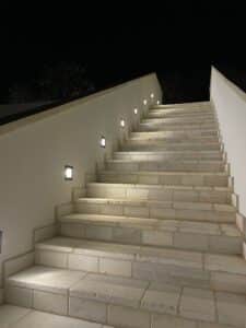 HAWO zeigt einen Stiegenaufgang bei Nacht mit seitlich eingebauten flächenbündigen, quadratischen Leuchten.