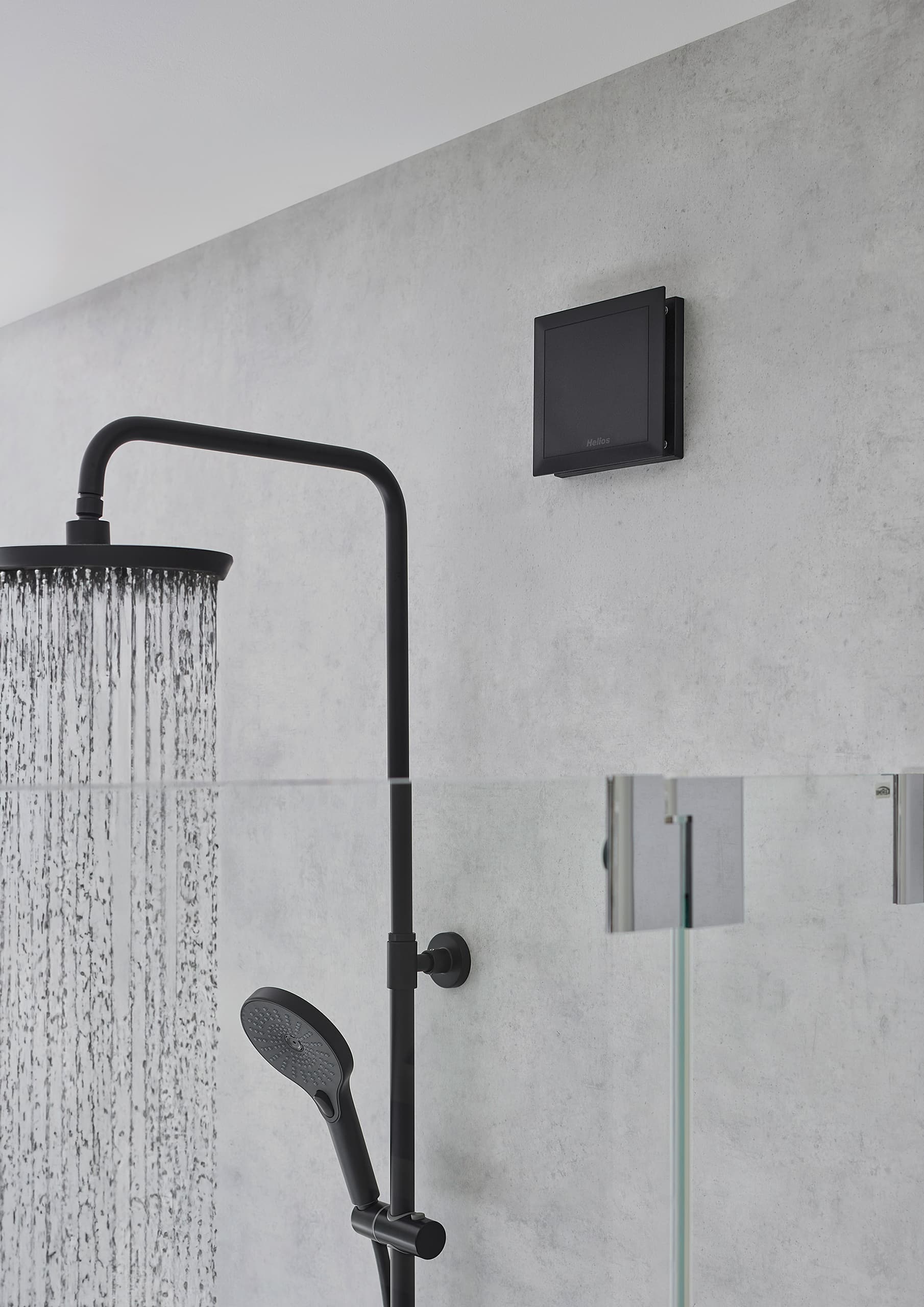 Helios zeigt eine Duschkkabine, in der das neue Designlüftungsventil in Schwarz an der Wand montiert ist.