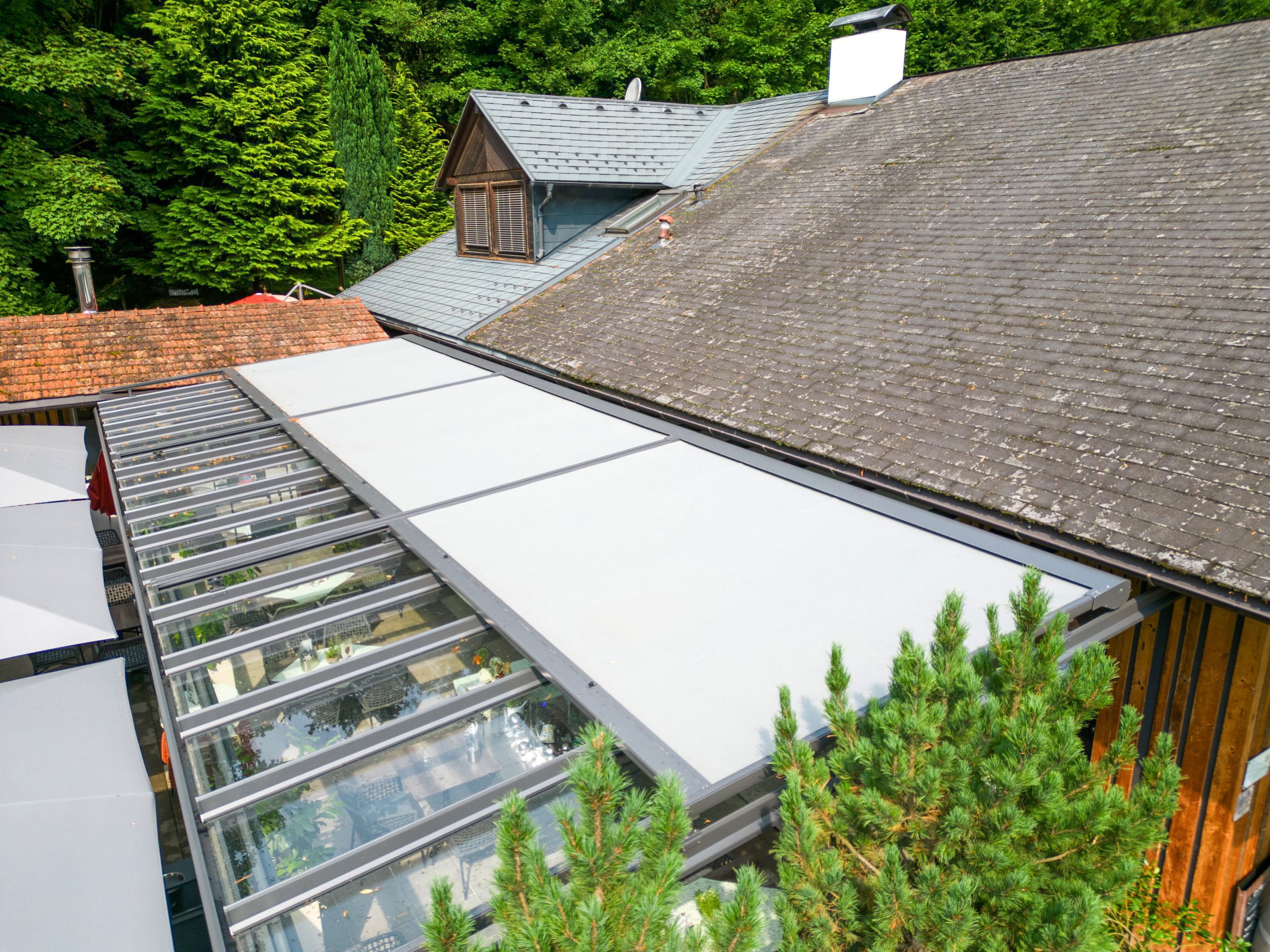 Ein Hof- bzw. Terrassenbereich mit einer Anbaupergola aus der Vogelperspektive mit Glasdach und integrierter Textilmarkise zur flexiblen Beschattung von HELLSAN.