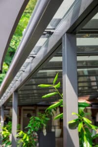 Detailaufnahme eines Terrassenbereichs mit Anbaupergola, Glasdach und integrierter Textilmarkise zur flexiblen Beschattung von HELLSAN.
