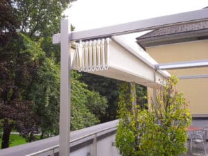 Eine freistehende Pergola mit gefaltetem bogenförmigen PVC-Faltdach, das für effektive Entwässerung sorgt mit patentiertem "FLY"-System mit Edelstahl-Pantografen der Marke Gibus Typ Isola Fly gezeigt von HELLSAN.