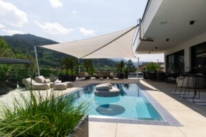 Ein modernes Sonnensegel mit drei Eckpfeilern und einer vierten Halterung am Wandvorsprung der Terrasse von SunFurl, gezeigt von HELLSAN.