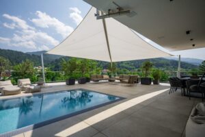 Ein modernes Sonnensegel mit drei Eckpfeilern und einer vierten Halterung am Wandvorsprung der Terrasse von SunFurl, gezeigt von HELLSAN.