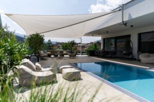 Ein modernes Sonnensegel mit drei Eckpfeilern und einer vierten Halterung am Wandvorsprung der Terrasse von SunFurl, gezeigt von HELLSAN.