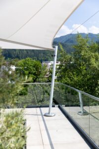 Ein modernes weißses Sonnensegel mit Eckpfeilern über Terrasse und Poolbereich von SunFurl, gezeigt von HELLSAN.