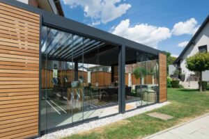 Pergola mit Lamaxa L60 Lamellendach von Warema mit Glasschiebetüren und Holzschiebeelementen zur Beschattung gezeigt von HELLSAN.