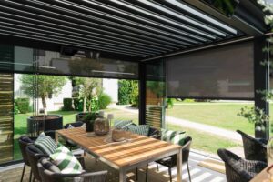 Eine Pergola mit Lamaxa L60 Lamellendach von innen mit Glasschiebetüren und äußeren Holzschiebeelementen die zur Beschattung - ein perfekter Sommer- bzw. Wintergarten von Warema, gezeigt von HELLSAN.