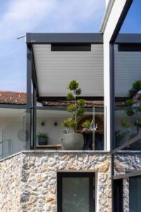 Eine moderne an die Hauswand gebaute schwarze Pergola mit weissem geschlossenen Lamellendach von Warema, gezeigt von HELLSAN.